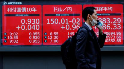 A man walks past an electronic board displaying Japan's 10-year government bonds level, the current Japanese Yen exchange rate against the U.S. dollar and Nikkei share average, outside a brokerage in Tokyo, Japan.