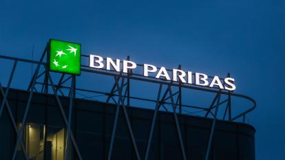 A glowing sign of BNP Paribas atop a building at night.