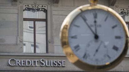 The Credit Suisse logo on the side of a building, with a clock in the foreground.