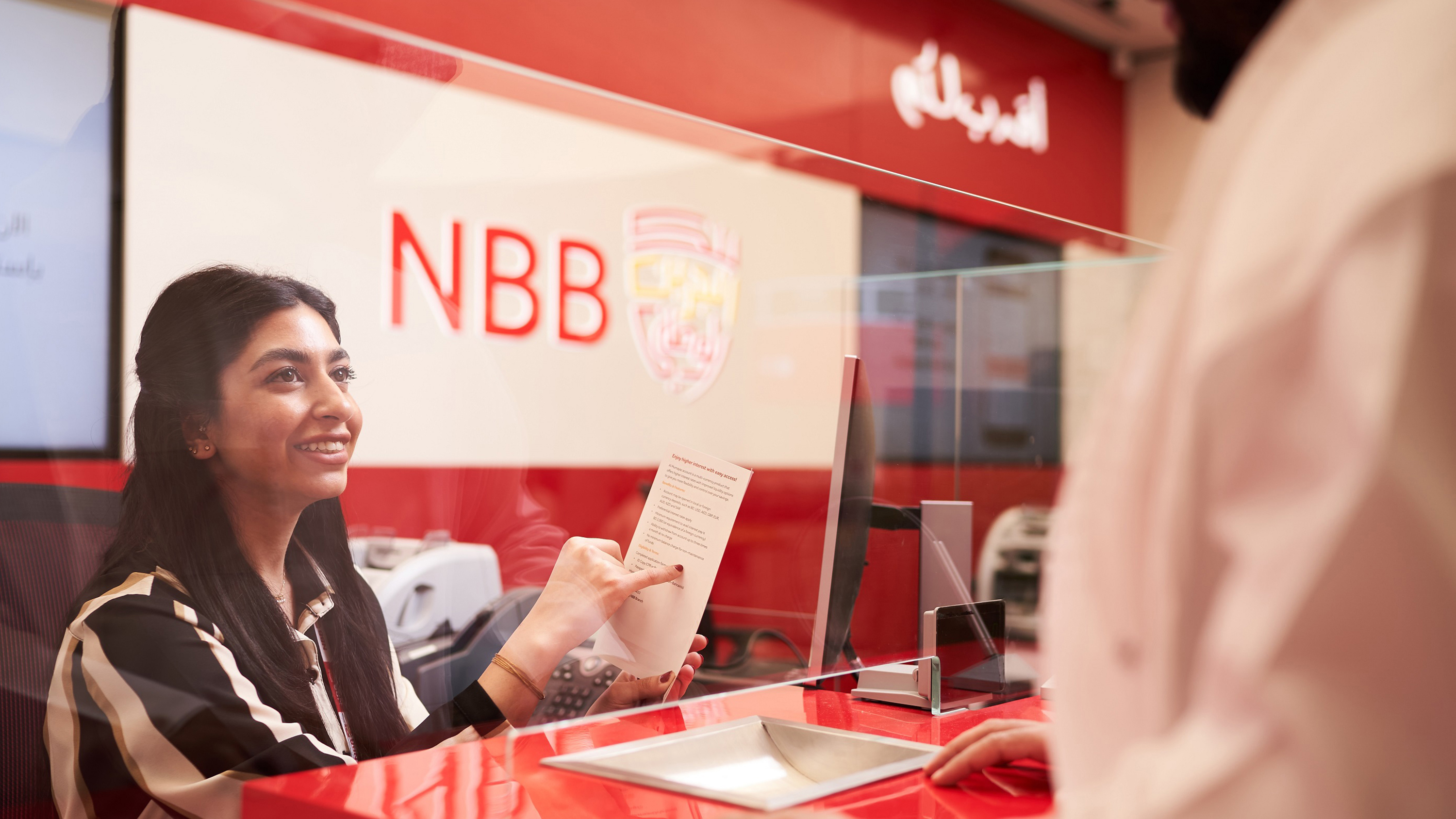 A woman sitting in a branch of NBB, pointing to a leaflet.