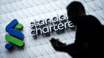 A silhouetted figure passes by a Standard Chartered sign